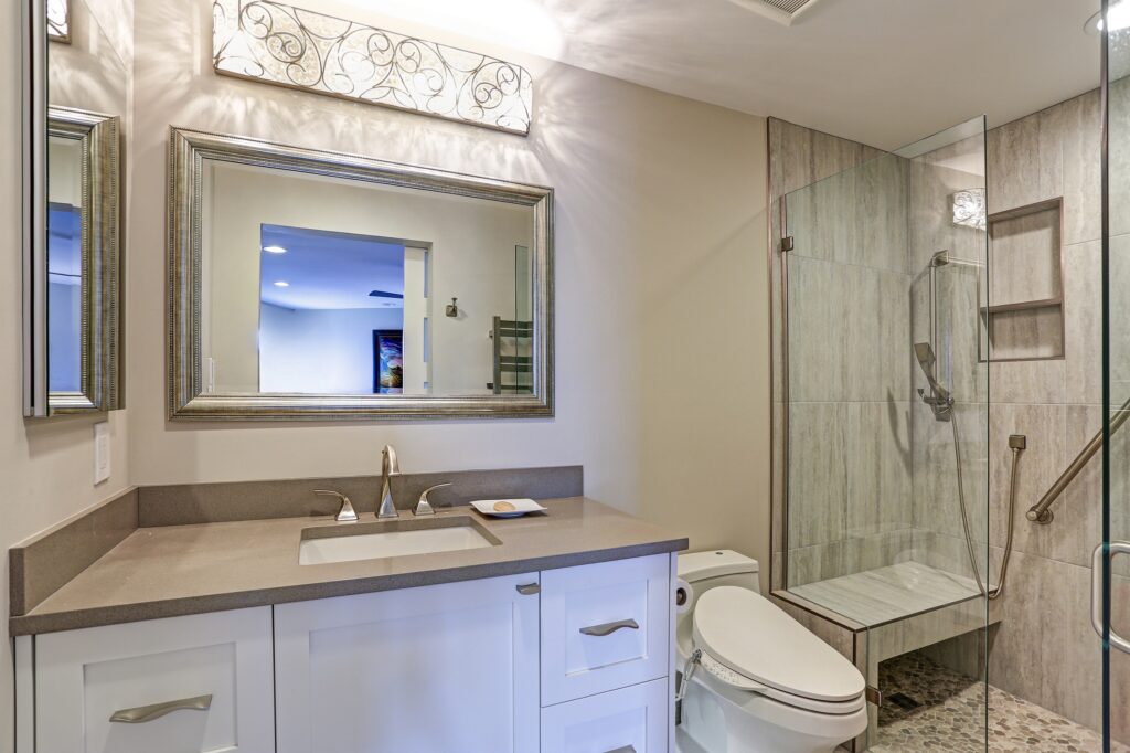 Contemporary bathroom design boasts white bathroom cabinet with taupe Quartz countertop, silver beaded mirror and modern polished chrome faucet lit by decorative lights.